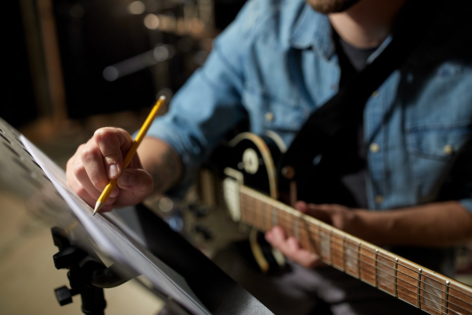 man with guitar writing to music book at studio